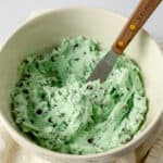 A small wooden spatula in a bowl of homemade mint chip buttercream.
