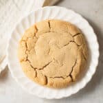 A single peanut butter cookie on a white scalloped plate.