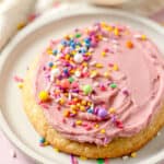 Colorful sprinkles on a pink-frosted single sugar cookie.