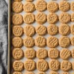 A baking tray filled with mini peanut butter cookies and a blue linen cloth underneath.
