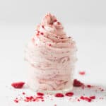 Light pink strawberry whipped cream piped in a swirl into a small mason jar and topped with lots of freeze dried strawberry crumbs.
