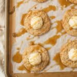 Oatmeal cookies on a baking sheet topped with vanilla mousse and caramel drizzle.