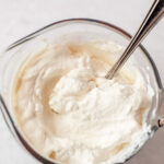 Stirring a measuring cup of homemade whipped cream with a spoon.
