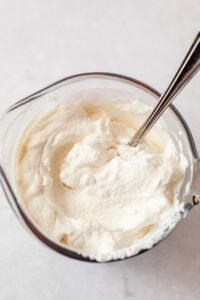Stirring a measuring cup of homemade whipped cream with a spoon.