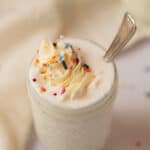 Vanilla milkshake in a small mason jar topped with whipped cream and sprinkles.