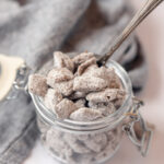 A flip-top glass jar filled with chocolate-peanut butter chex mix and a spoon.