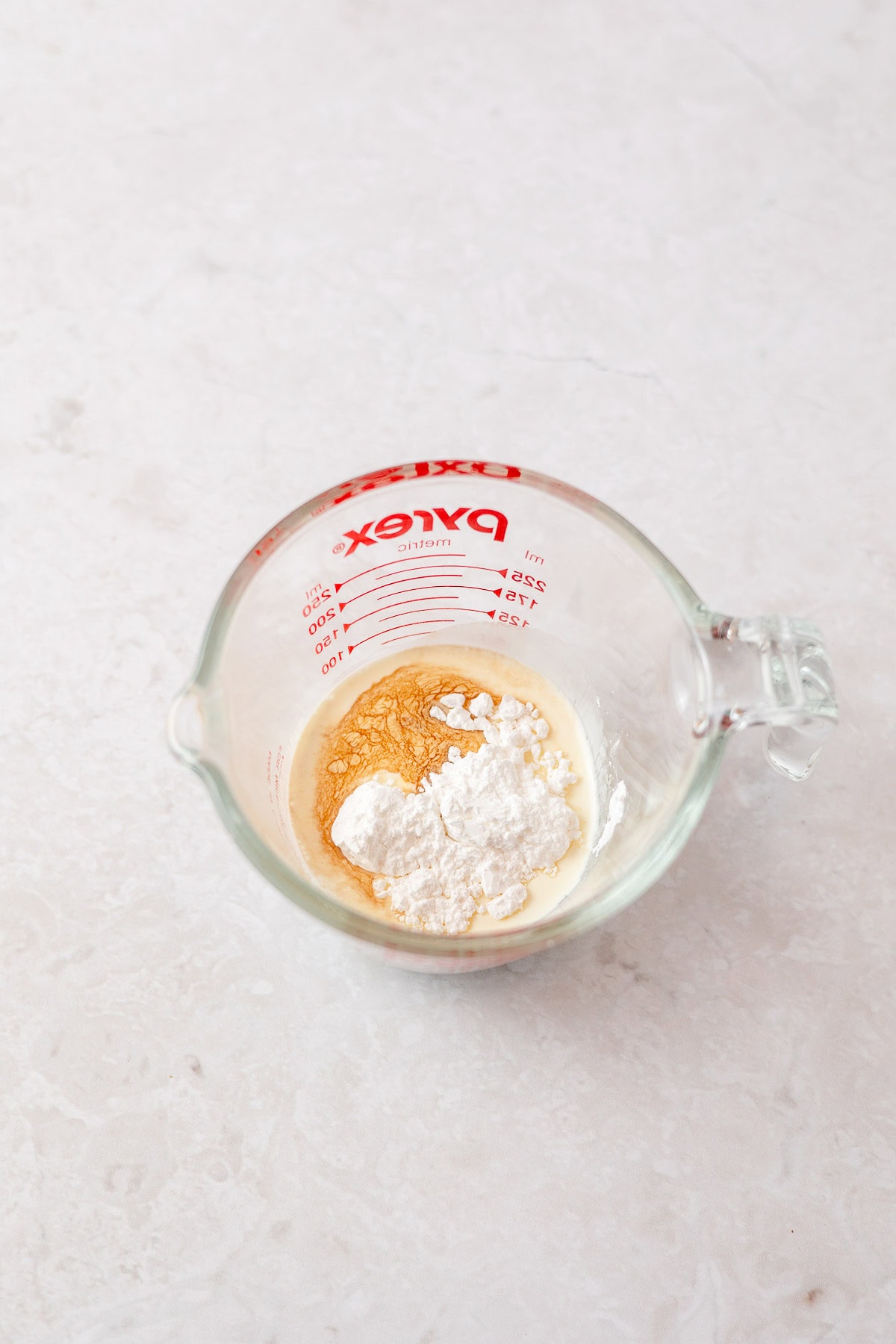 A glass measuring cup filled with whipped cream, powdered sugar, and vanilla extract.