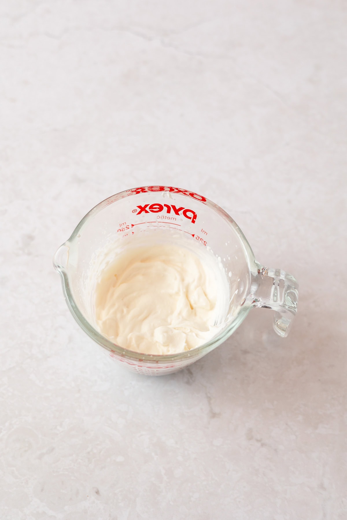 A glass measuring cup filled with a small amount of whipped cream.