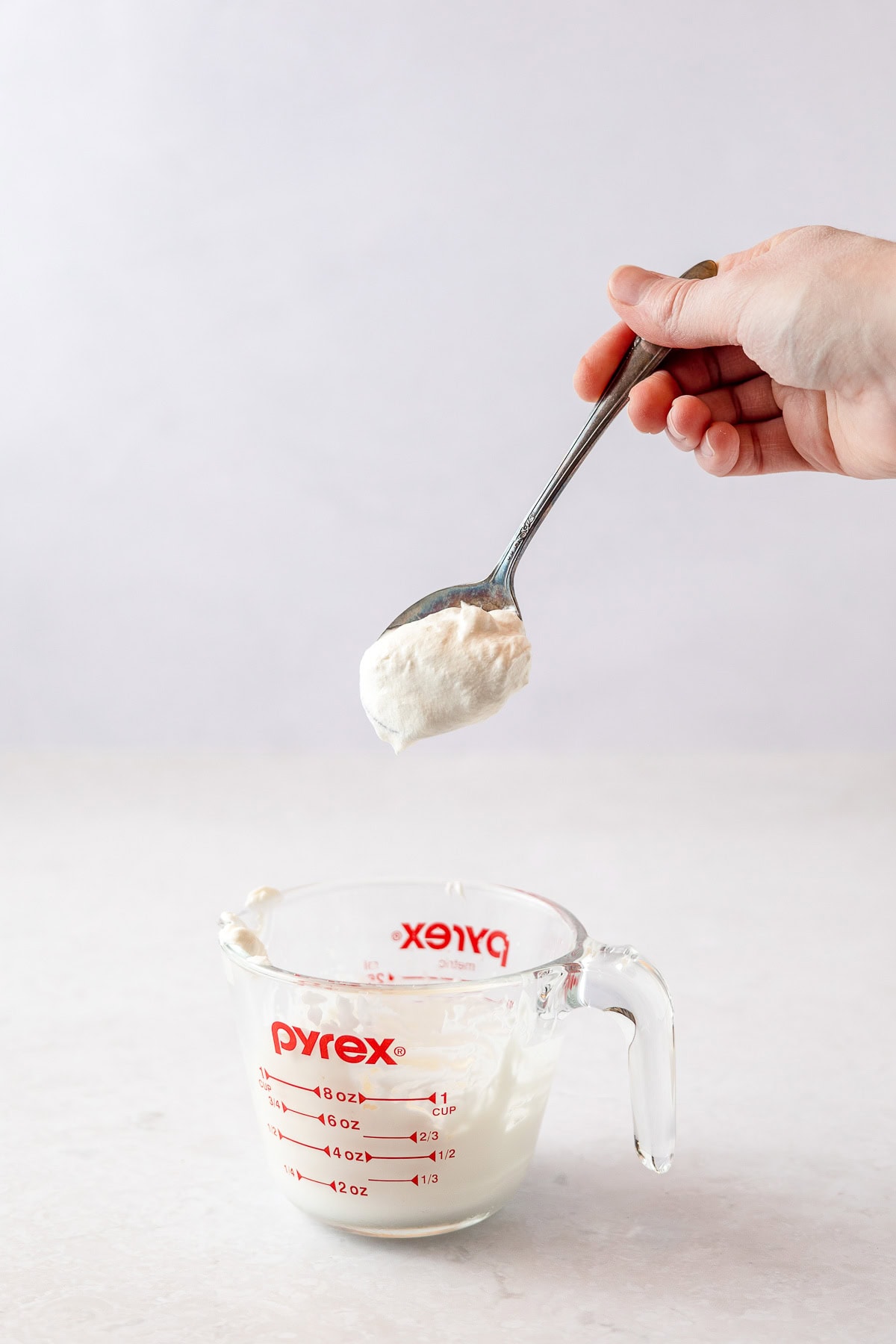Lifting a spoonful of whipped cream out of a glass measuring cup.