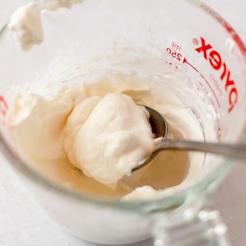 Spooning whipped cream out of a glass measuring cup.