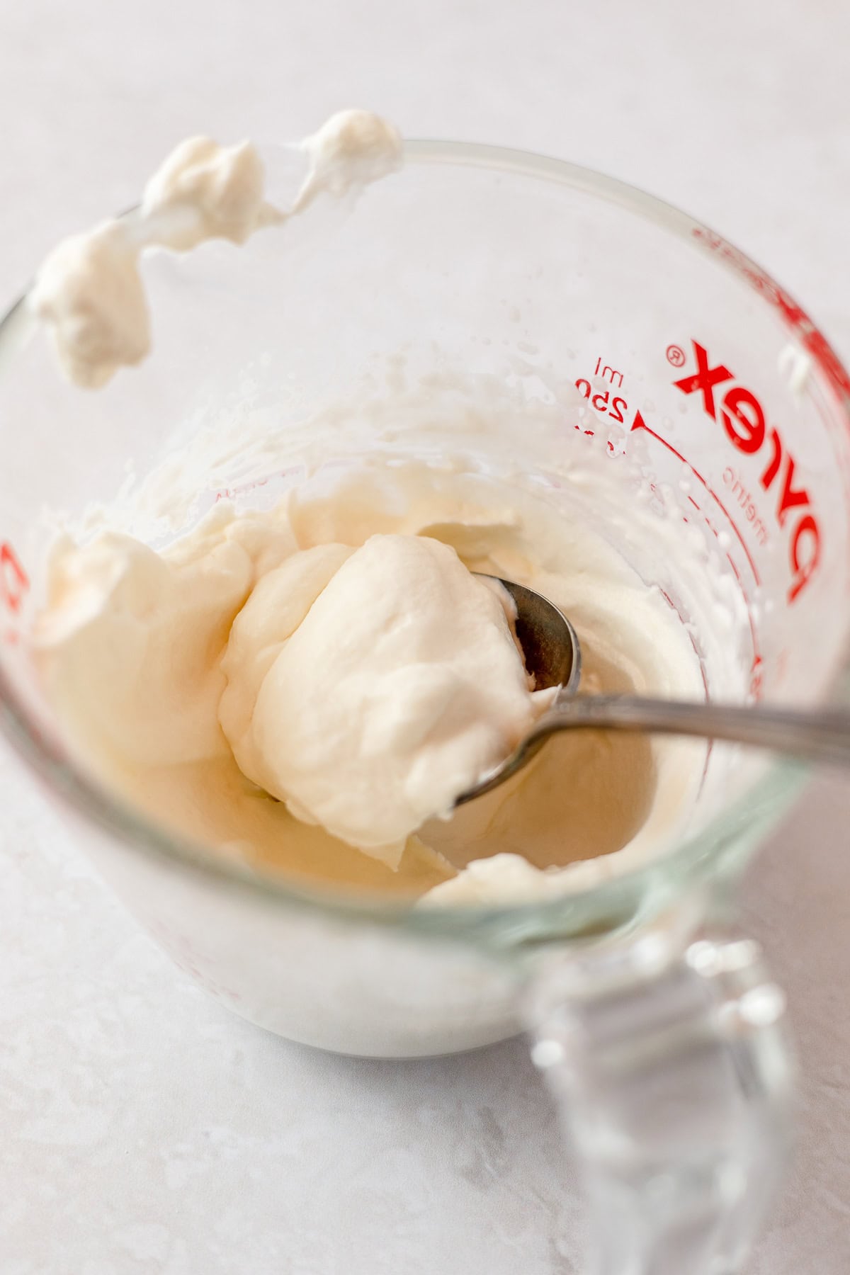 Spooning whipped cream out of a glass measuring cup.