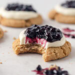A homemade blueberry cheesecake cookie with a bite removed.