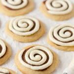 Cinnamon roll cookies with cinnamon sugar layer and swirl of piped cream cheese frosting.