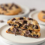 A cookie filled with semi-sweet chocolate chunks, broken in half and stacked on a small plate.