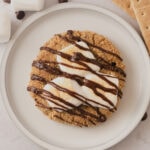 A large s'mores cookie on a plate with marshmallows and a chocolate drizzle on top.