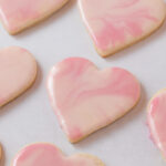Iced marbled heart sugar cookies arranged in rows on parchment paper.