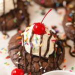 A brownie-cookie with vanilla mousse, chocolate drizzles, sprinkles and a maraschino cherry on top.
