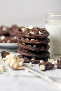 A stack of chocolate cookies with a spoonful of white chips in front.