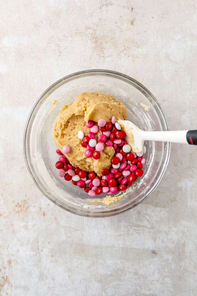 A bowl of cookie dough with pink, red, and white coated candies.