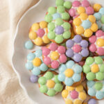 A white plate filled with cookies decorated with pastel M&Ms in the shape of flowers.