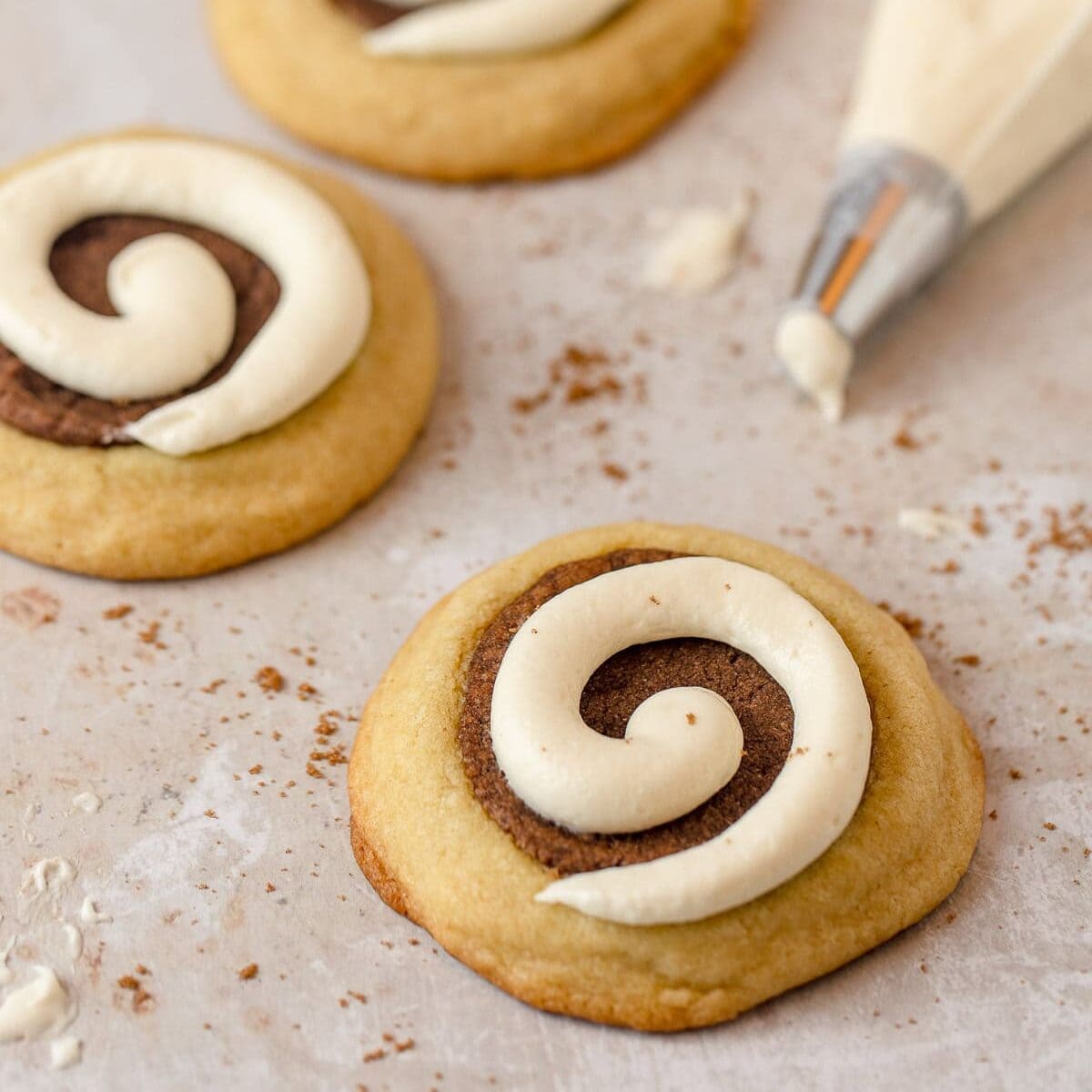 Cinnamon roll cookies with cream cheese frosting on top of brown sugar crusted cookies.