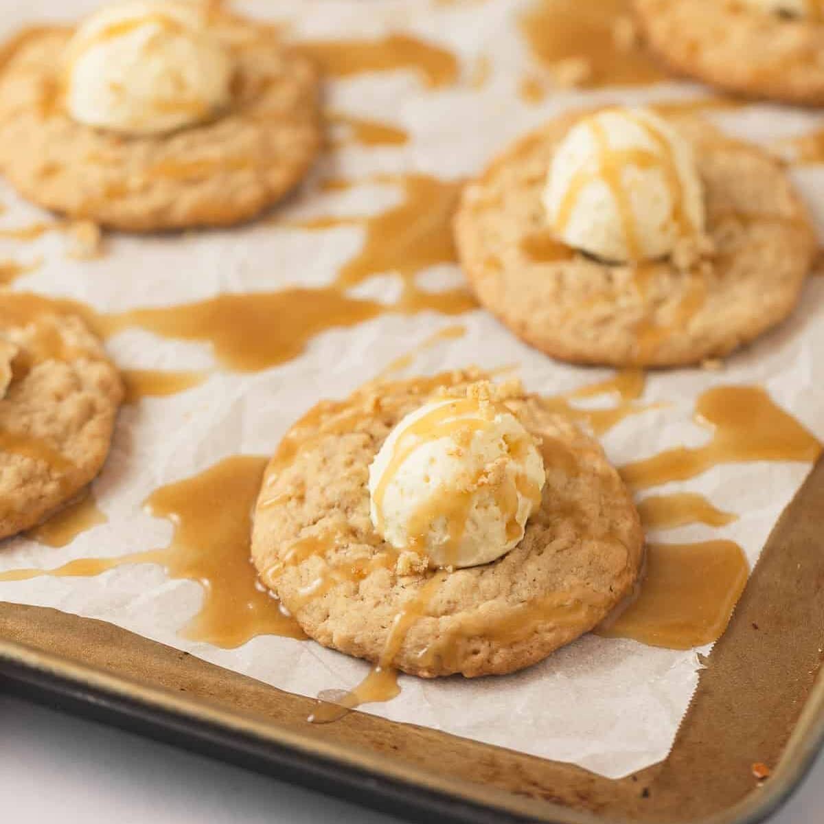 Oatmeal cookies on a baking sheet with scoops of vanilla mousse and drizzles of caramel sauce.