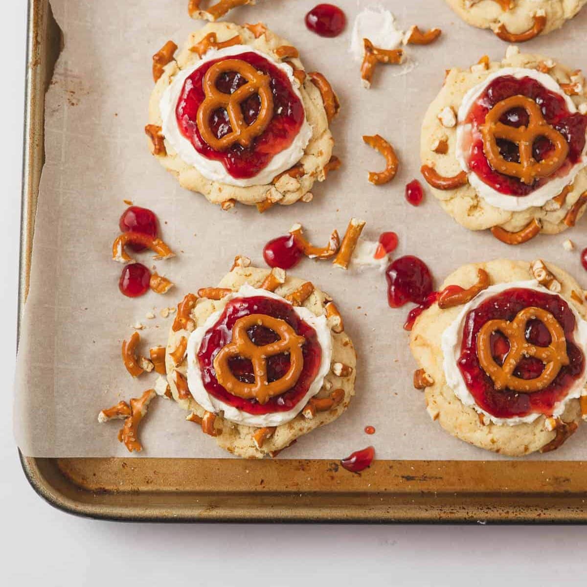 Decorated sugar cookies with pretzels, a creamy whipped topping, strawberry jam, and a pretzel on top.