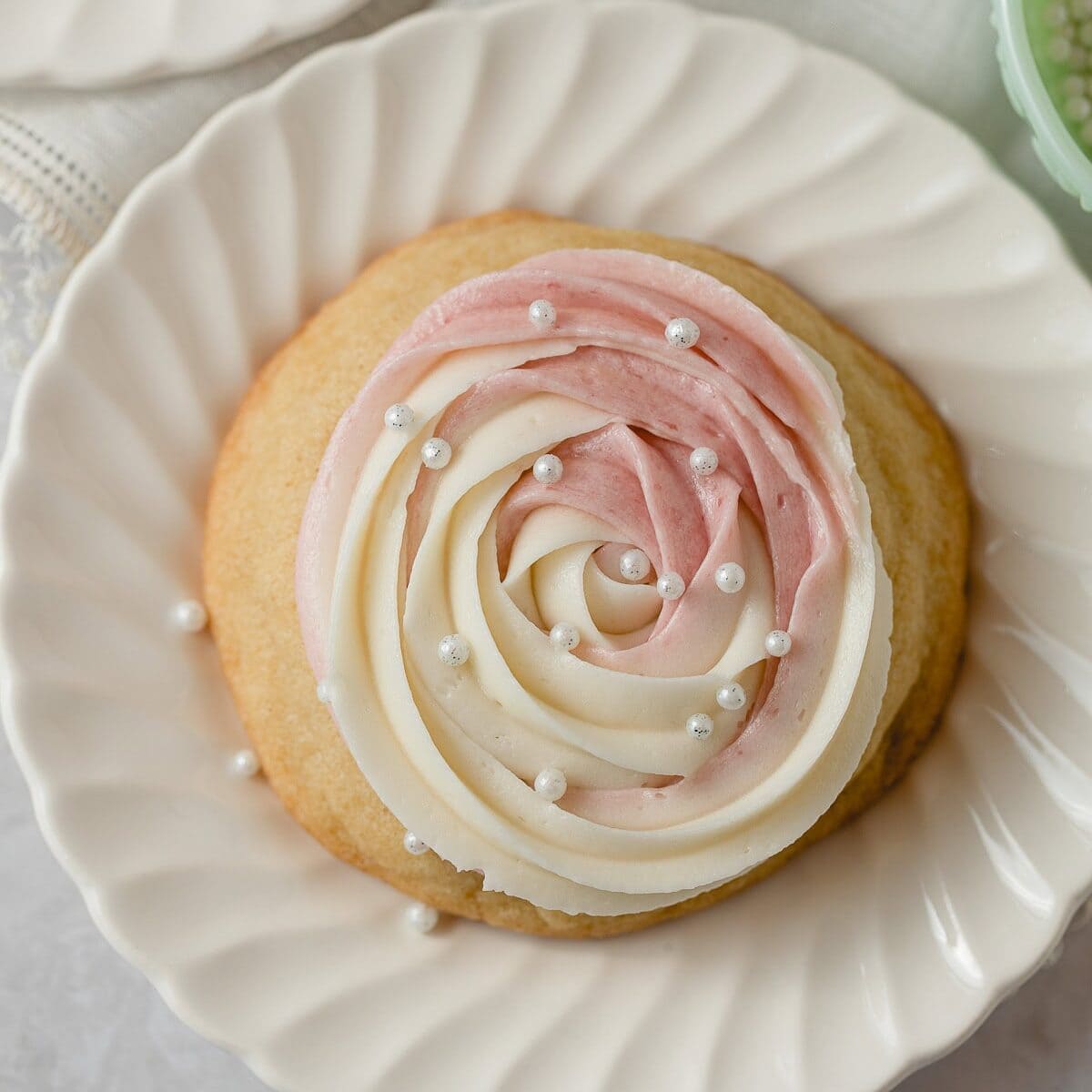A sugar cookie topped with a swirl of pink and white buttercream and topped with edible pearl sprinkles.