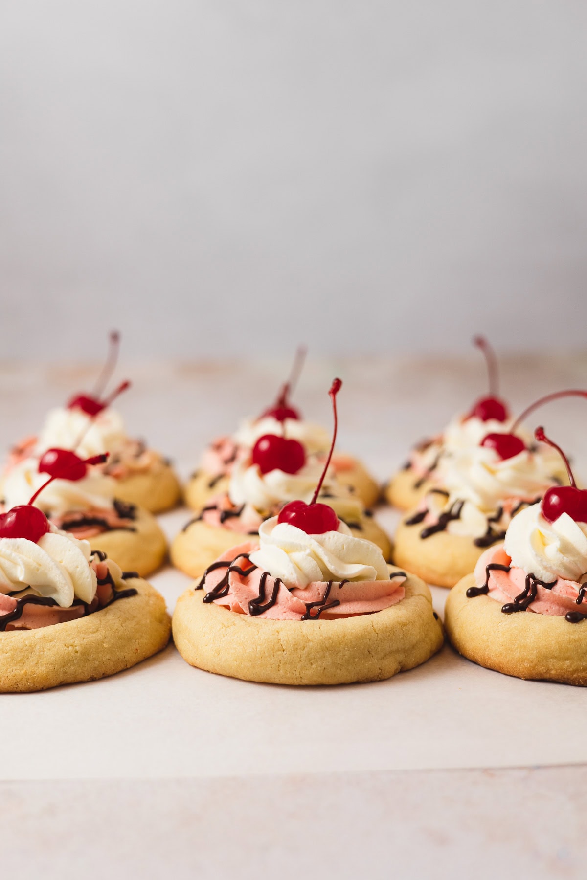 Rows of Banana Split cookies topped with strawberry and banana mousse, whipped cream, and a cherry on top.