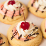 A Banana Split Cookie topped with strawberry and banana mousse, whipped cream, and a cherry on top.