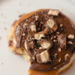 A Caramel Shortbread cookie topped with caramel, milk chocolate, and Twix bar chunks with a bite removed.