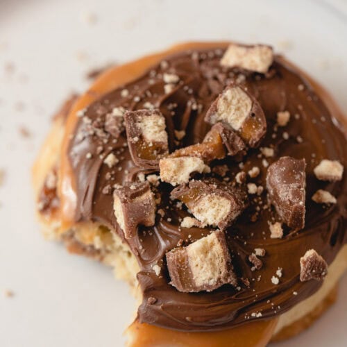 A Caramel Shortbread cookie topped with caramel, milk chocolate, and Twix bar chunks with a bite removed.