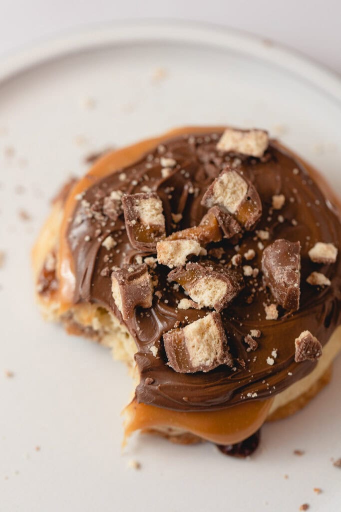 A Caramel Shortbread cookie topped with caramel, milk chocolate, and Twix bar chunks with a bite removed.