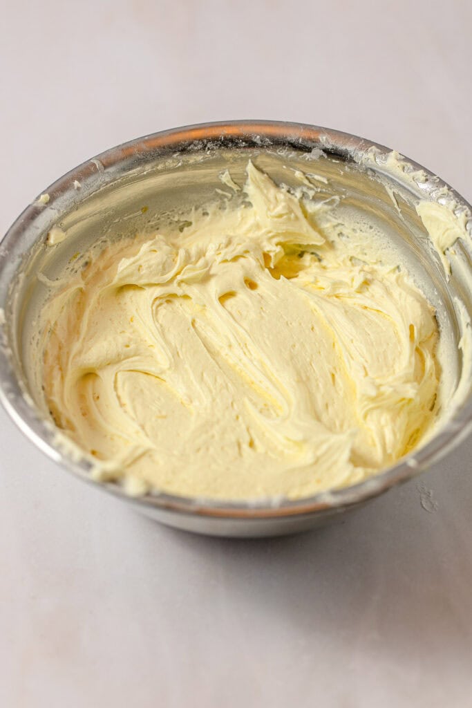 A metal bowl with light yellow lemon frosting swirled inside.