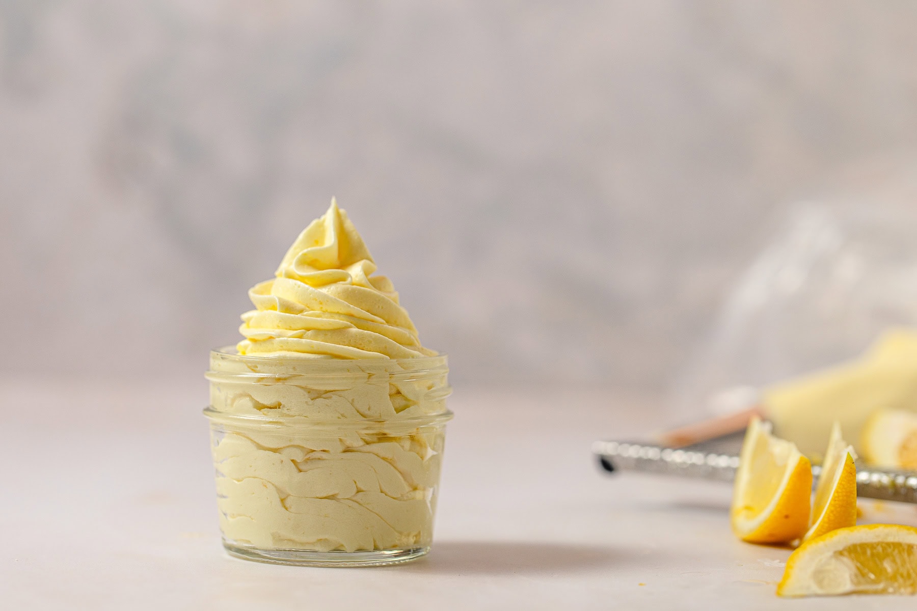 A mason jar filled with piped light yellow lemon frosting with lemon slices nearby.