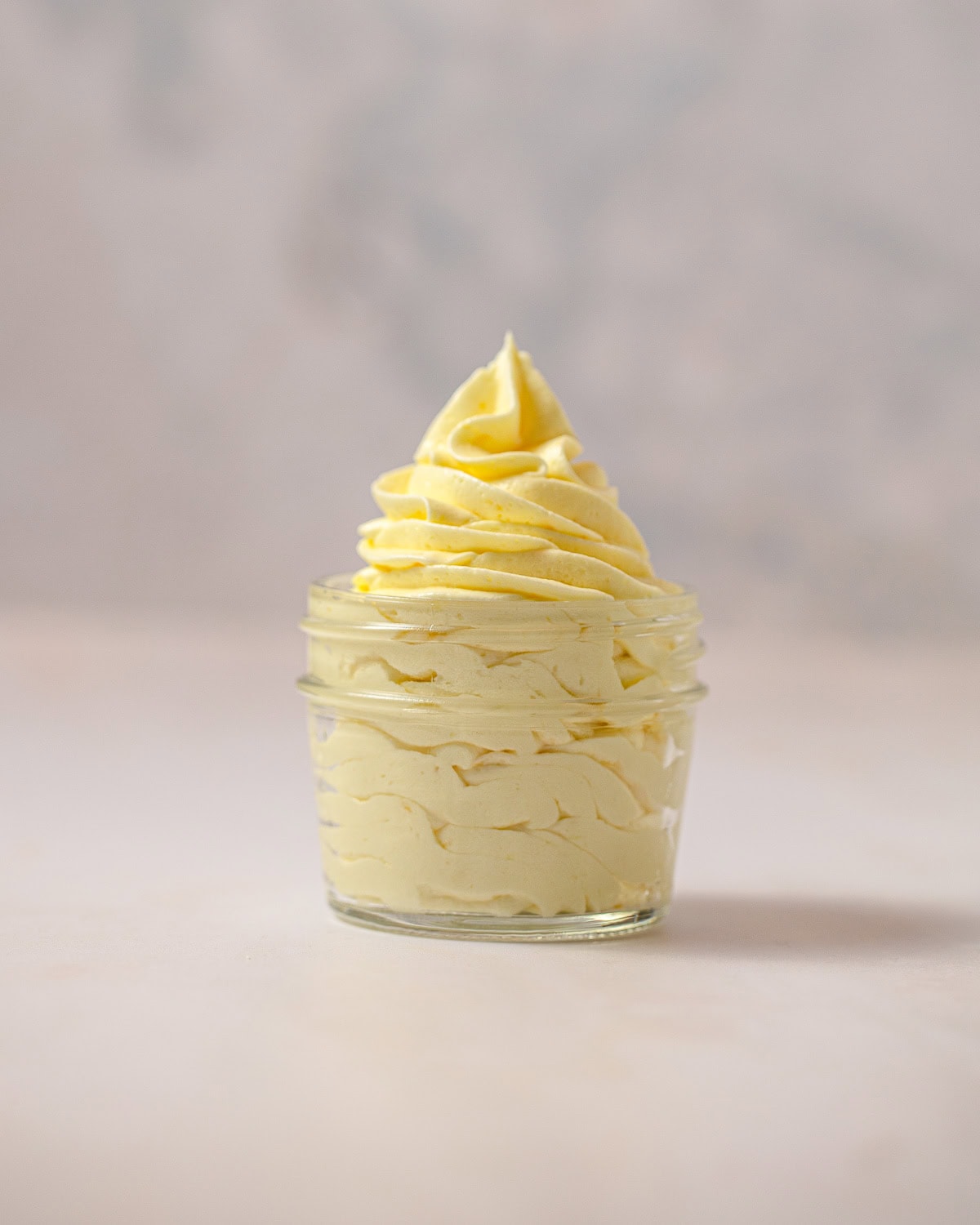 A mason jar filled with piped light yellow lemon frosting.
