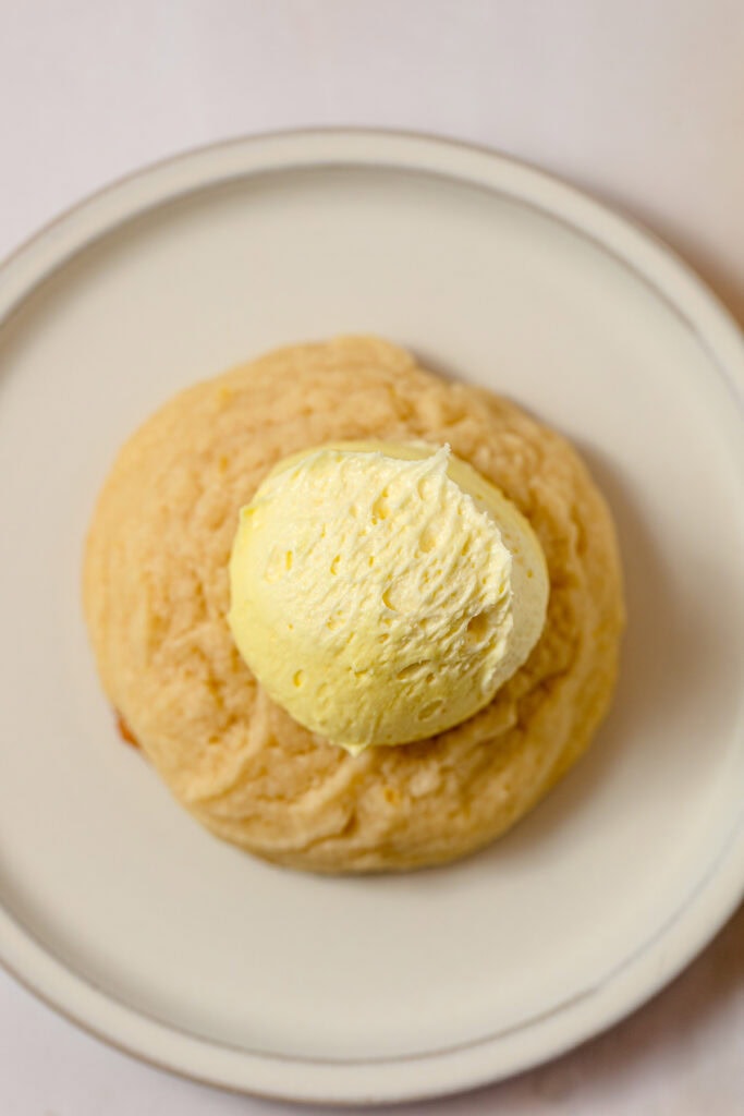 A sugar cookie topped with a scoop of yellow lemon frosting.