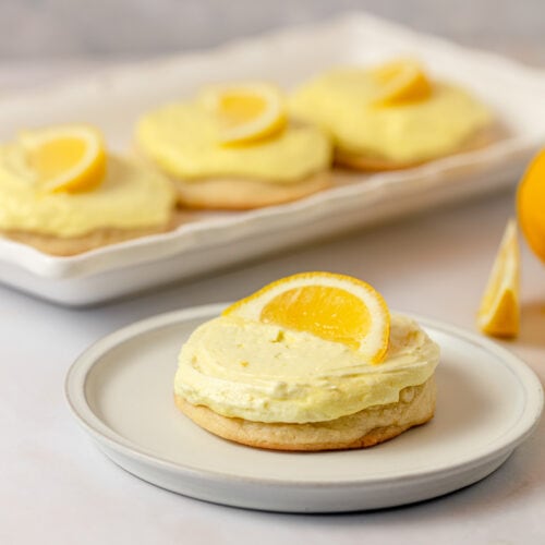 A lemonade cookie with yellow frosting and lemon slice on a plate.