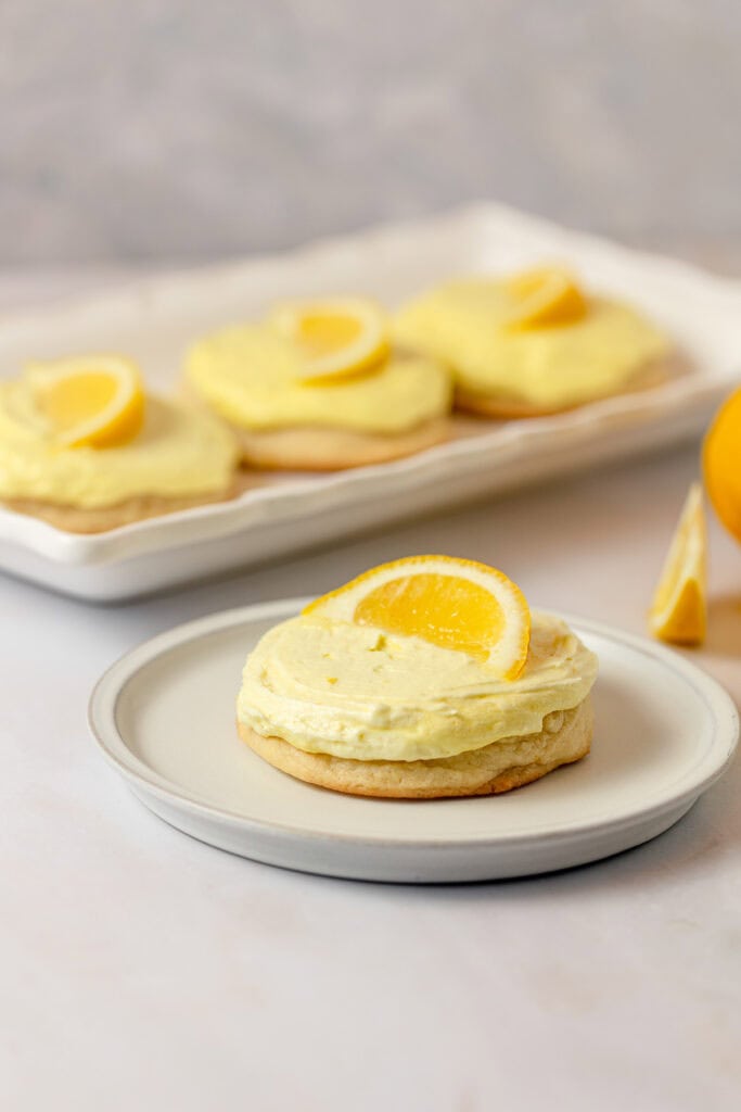A lemonade cookie with yellow frosting and lemon slice on a plate.