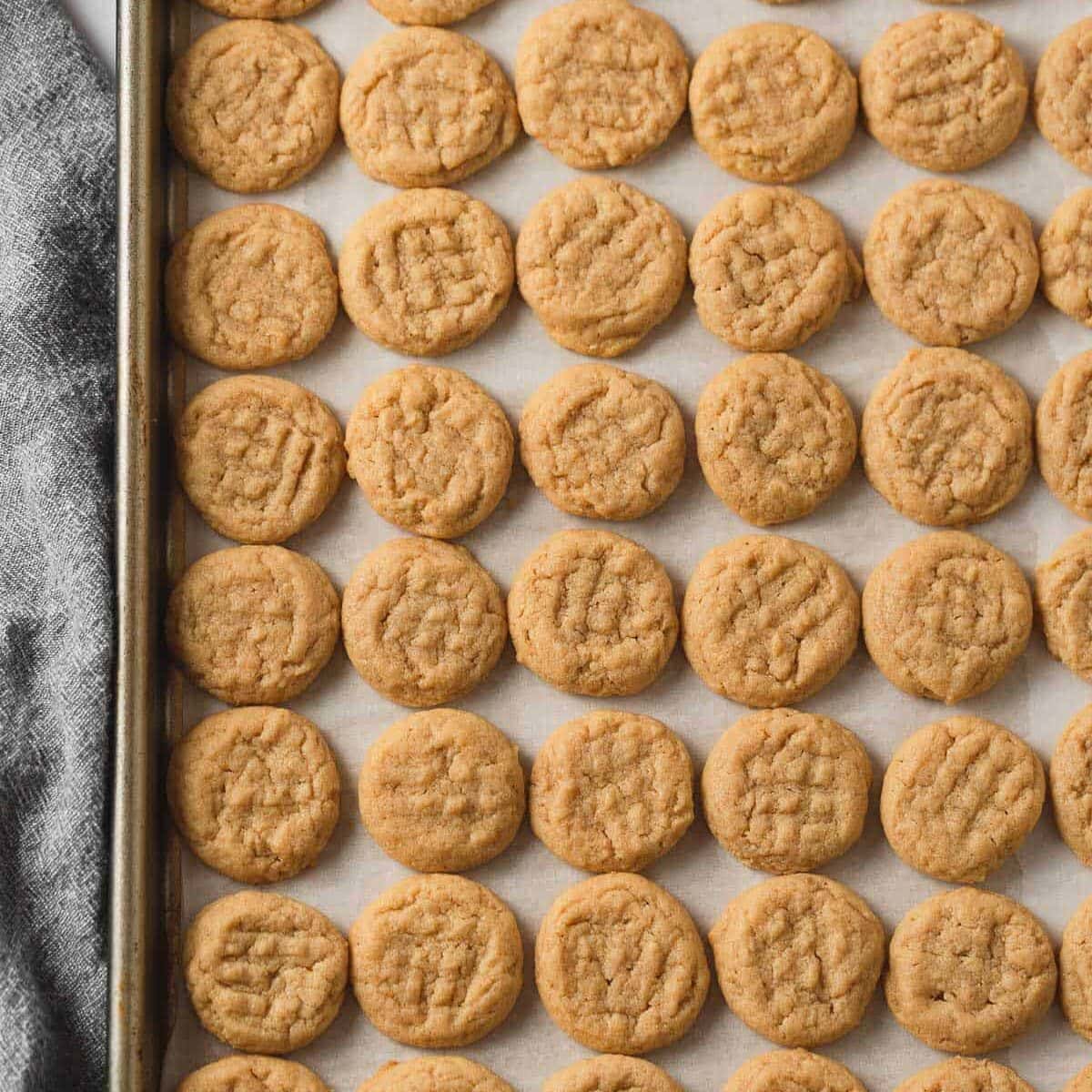 A baking tray filled with mini peanut butter cookies and a blue linen cloth underneath.