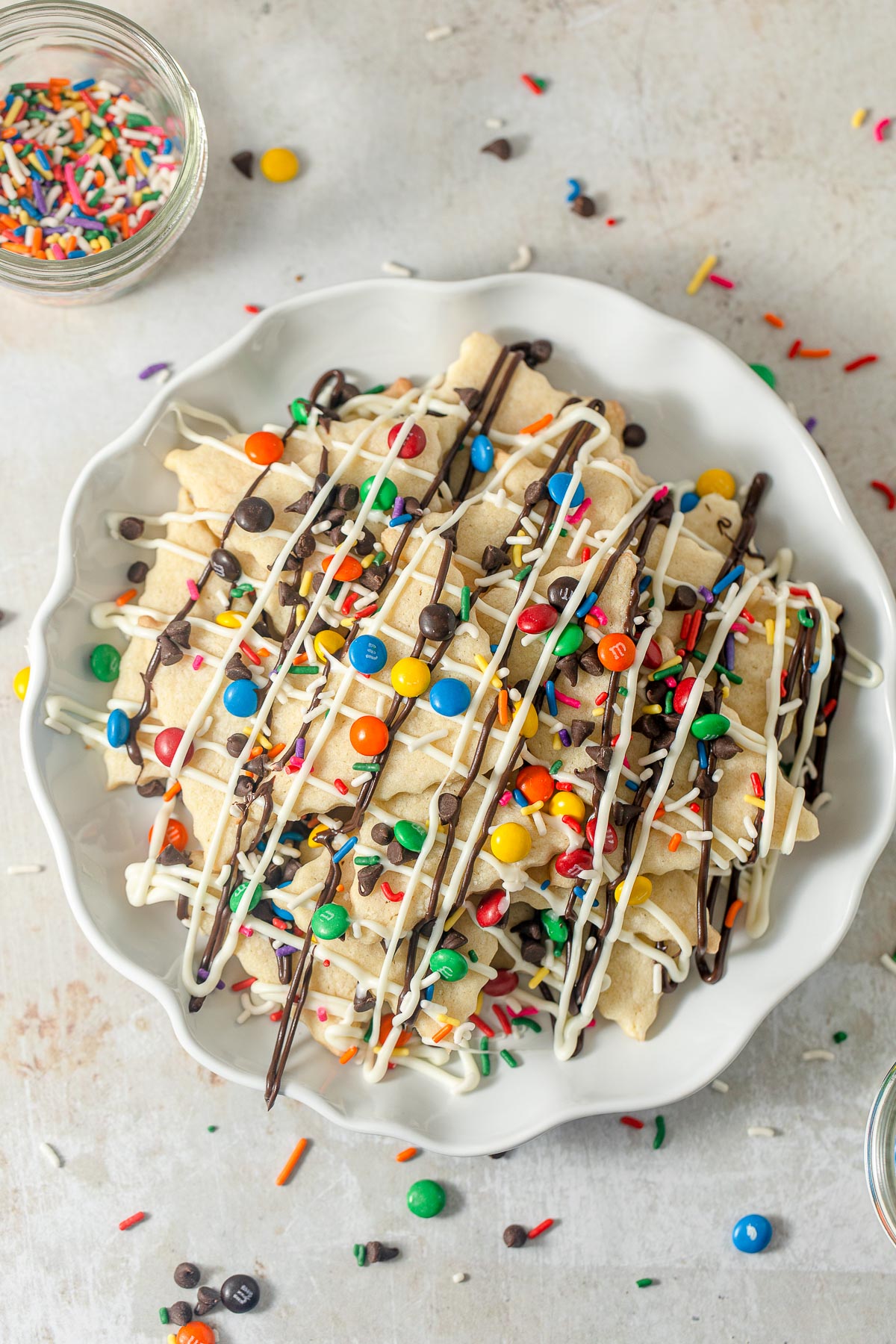 A plate of homemade sugar cookies cut into triangles and layered with drizzles of chocolate and candy-covered chocolate drops.