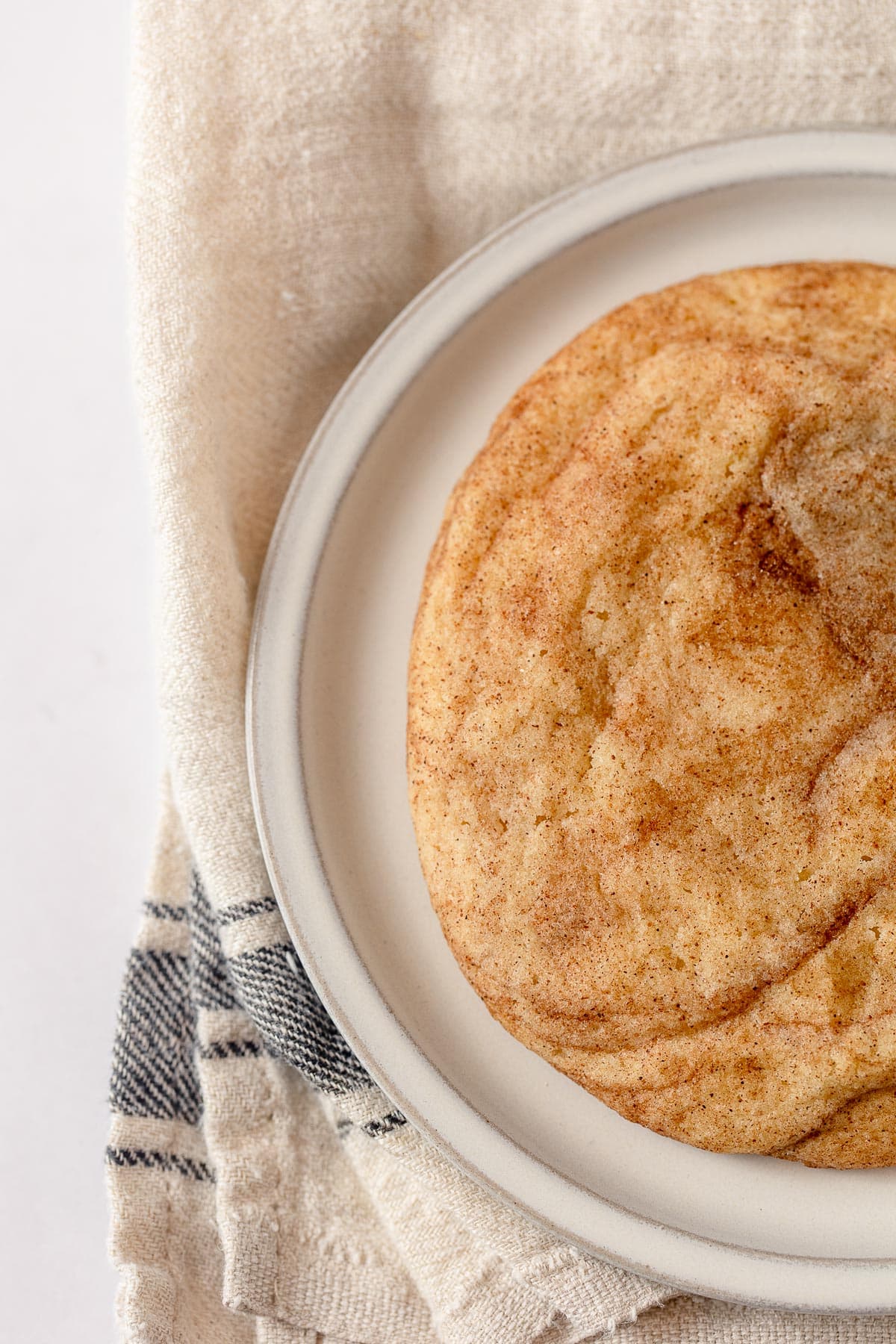 A cinnamon-sugar cookie on a plate with a farmhouse towel.