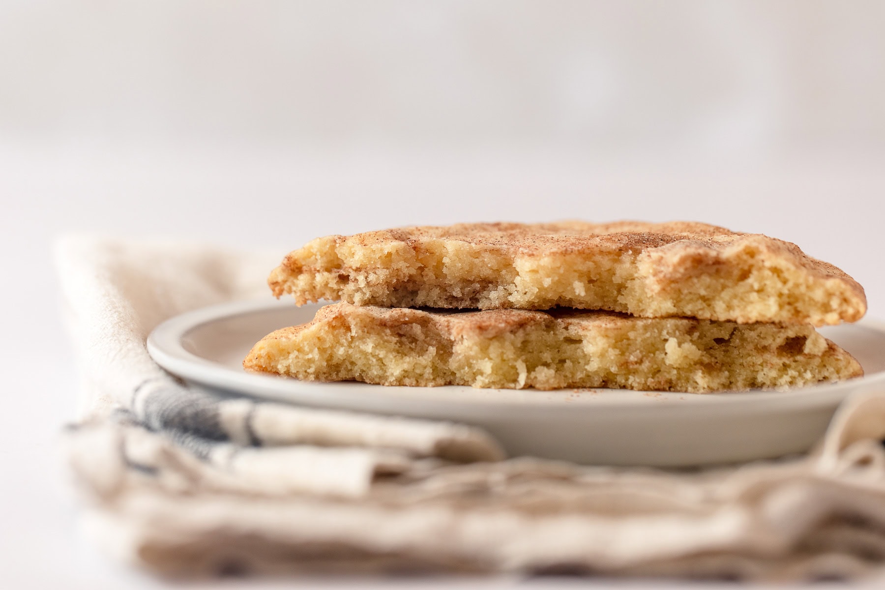 Two halves of a snickerdoodle cookie stacked on a plate with a farmhouse towel underneath.