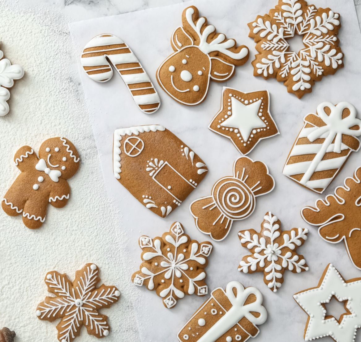 A variety of cut-out gingerbread shapes (gingerbread men, houses, snowflakes, stars, gifts, and candies) decorated with finely piped white icing.