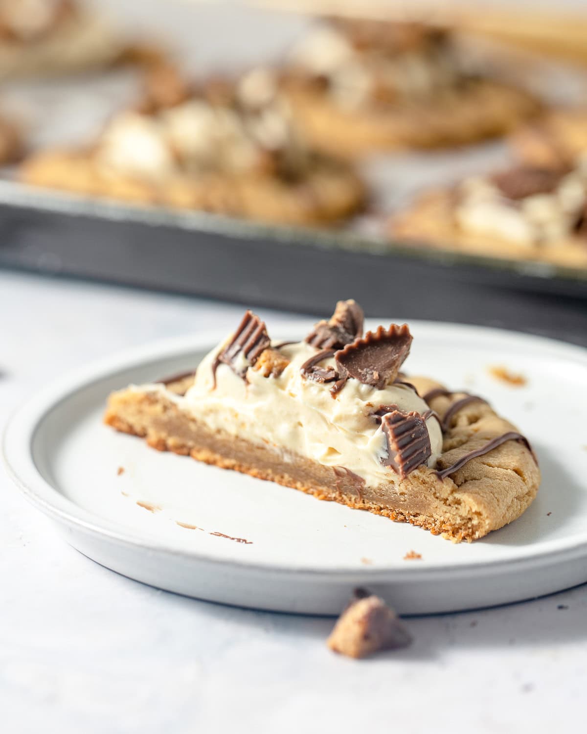 Half of a peanut butter cookie topped with a scoop of peanut butter mousse, drizzles of milk chocolate and pieces of crushed peanut butter cups.