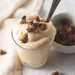 A small glass filled with peanut butter mousse topped with chunks of peanut butter cups with a vintage spoon tucked inside the glass.