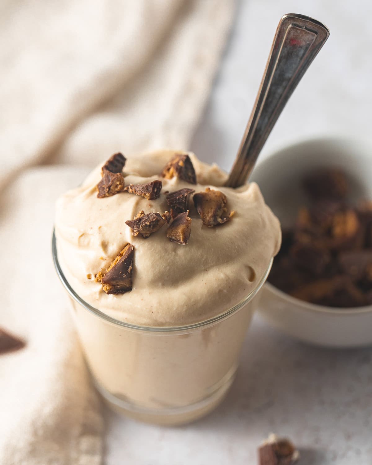 A small glass filled with peanut butter mousse topped with chunks of peanut butter cups with a vintage spoon tucked inside the glass.