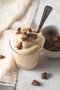 A small glass filled with peanut butter mousse topped with chunks of peanut butter cups with a vintage spoon tucked inside the glass.