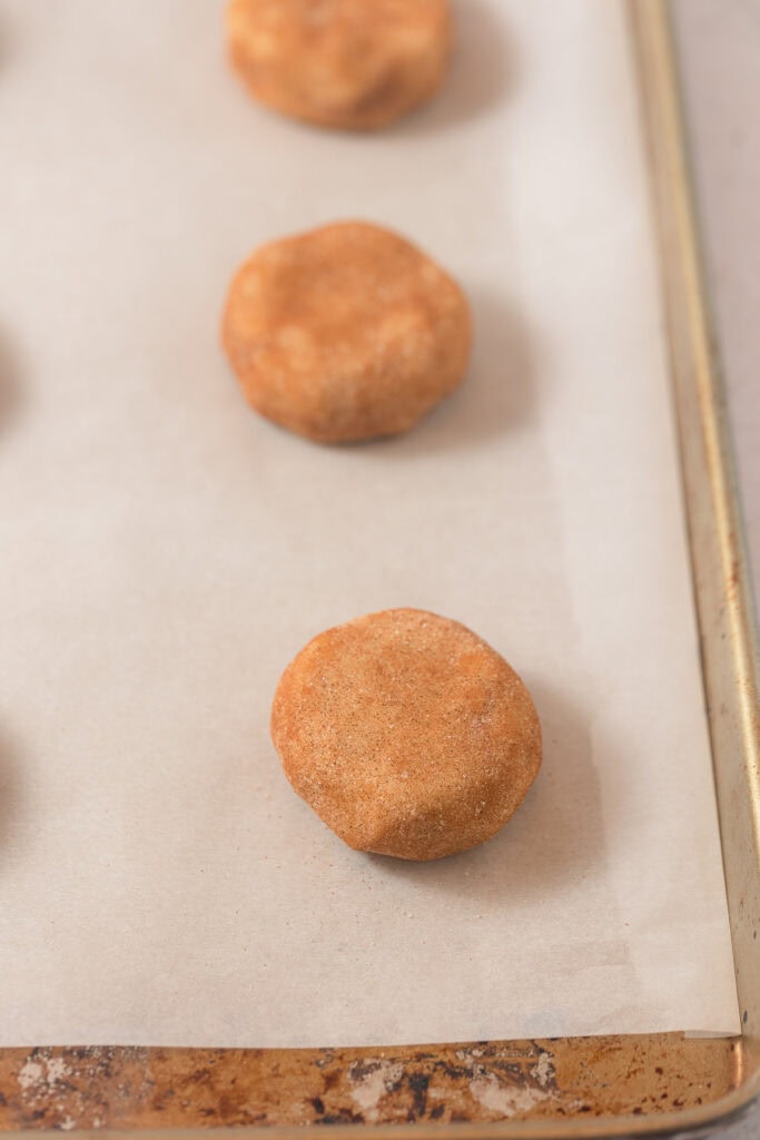 Disks of cinnamon-sugar dough on a parchment-lined baking tray.