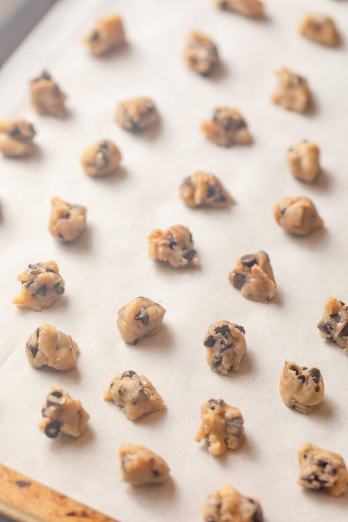 Mini scoops of chocolate chip cookie dough on a parchment-lined baking sheet.